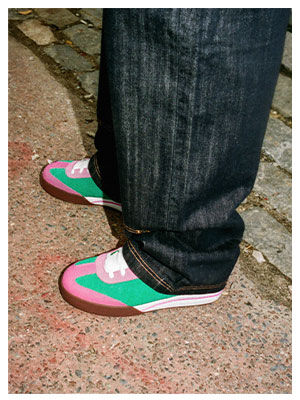 Modelo con jeans oscuros calzando tenis skate Reebok x IceCream Board Flip en combinaci&oacute;n verde rosa y blanco con suela caf&eacute;, sobre pavimento texturizado con adoquines grises, estilo urbano diurno.