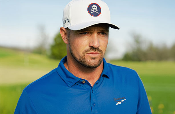 Modelo Reebok Golf con polo azul, gorra blanca con parche calavera y logo vector, campo de golf de fondo.