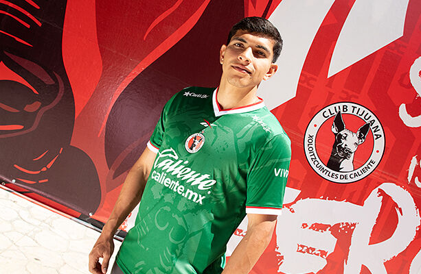 Modelo Reebok x Xolos en jersey verde frente a mural rojo del club.