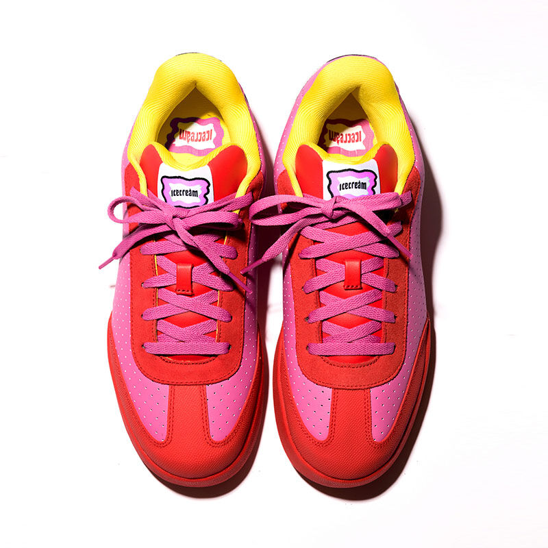 Vista cenital del par de tenis skate Reebok x IceCream Board Flip en tonos rosa rojo y amarillo ne&oacute;n con cordones morados, leng&uuml;eta con logo, sobre fondo blanco, dise&ntilde;o sim&eacute;trico, acabado premium.