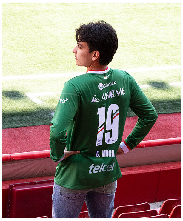 Modelo Reebok x Xolos en jersey verde frente a mural rojo del club.