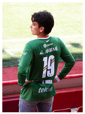 Modelo Reebok x Xolos en jersey verde frente a mural rojo del club.