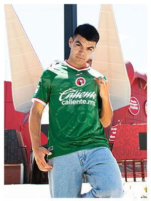Portrait Reebok x Xolos con modelo en jersey verde frente a estructura roja.