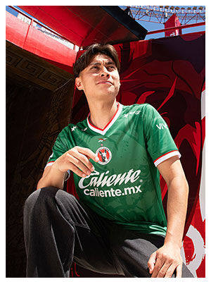 Card Reebok x Xolos con modelo en jersey verde sentado, mural rojo de fondo.