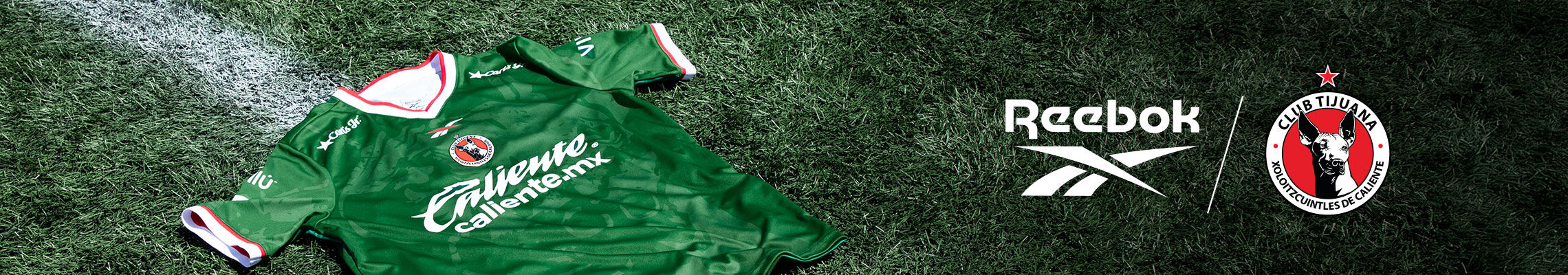 Banner horizontal con jersey verde manga corta Reebok x Club Tijuana extendido sobre c&eacute;sped del estadio Caliente, escudo Xoloitzcuintles, logo Reebok, branding Reebok y Club Tijuana en esquina superior derecha.