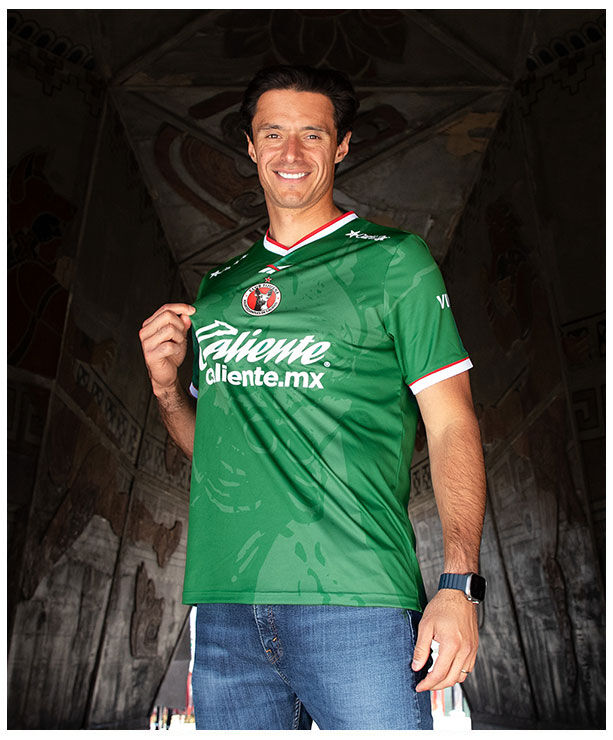 Portrait Reebok x Xolos con modelo en jersey verde, fondo estructura roja.