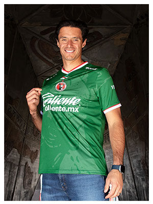 Portrait Reebok x Xolos con modelo en jersey verde, fondo estructura roja.