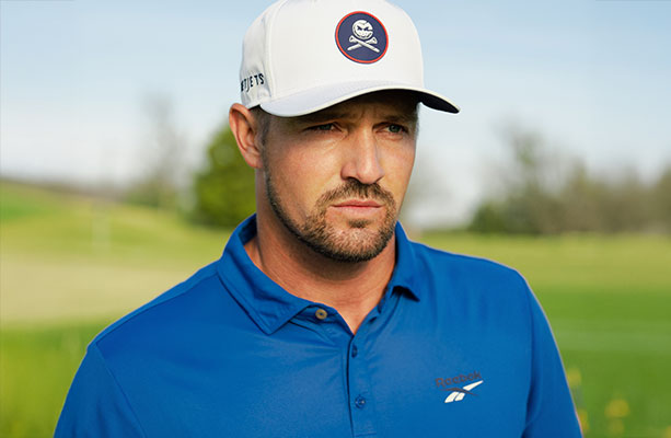 Modelo Reebok Golf con polo azul, gorra blanca con parche calavera y logo vector, campo de golf de fondo.