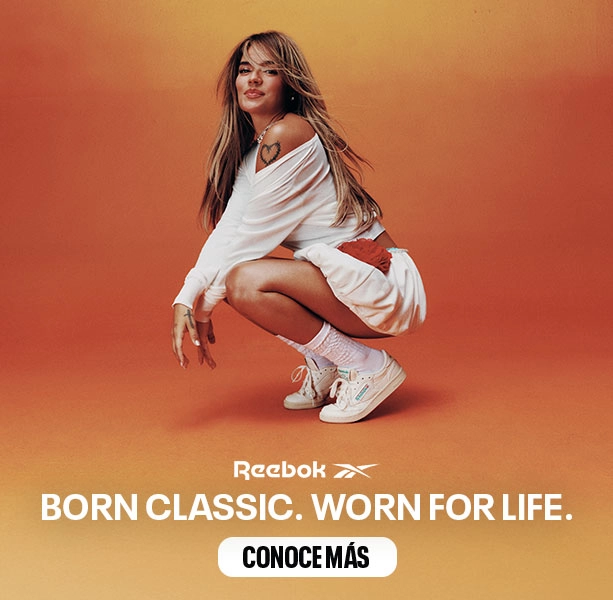 Banner desktop home Reebok x Karol G Born Classic Worn For Life, Karol G en cuclillas con conjunto blanco oversize y tenis Club C 85 blancos, par de tenis Club C 85 en primer plano sobre fondo naranja, logo Reebok Vector y bot&oacute;n Conoce M&aacute;s. Reebok, Karol G, Club C 85, tenis blancos Reebok, Reebok Classics y campa&ntilde;a Born Classic Worn For Life.