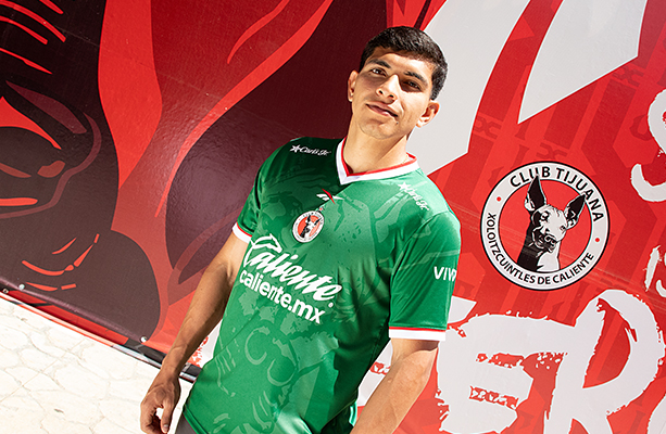 Modelo Reebok x Xolos en jersey verde frente a mural rojo del club.