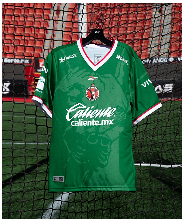 Reebok x Xolos en jersey verde frente a la porter&iacute;a rojo del club.