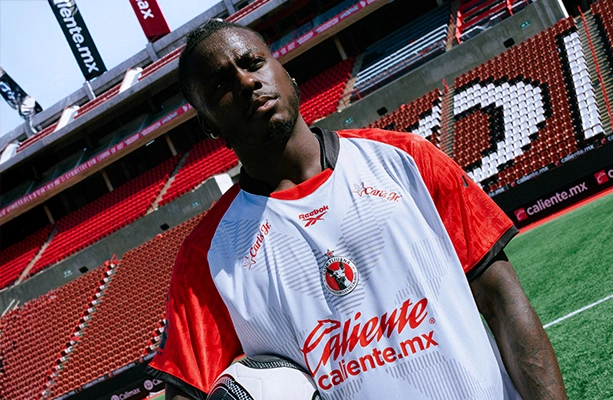 Modelo vistiendo jersey Reebok de Club Tijuana blanco con mangas rojas en el estadio