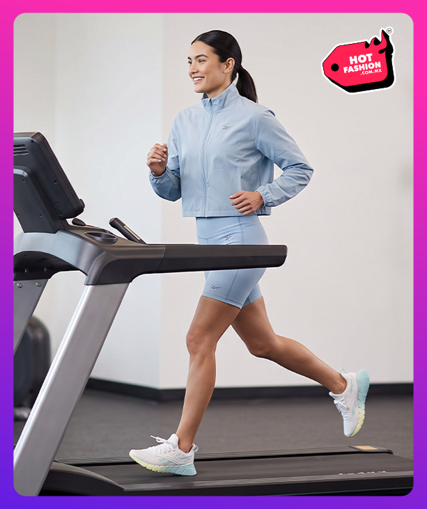 Look mobile Reebok Hot Fashion para mujer, modelo corriendo en caminadora con conjunto azul cielo Reebok de chamarra corta y short ciclista, tenis de running blancos Reebok, equipo de gimnasio de fondo, etiqueta Hot Fashion. Reebok mujer, ropa deportiva Reebok, conjunto deportivo, short ciclista, tenis blancos Reebok y rebajas Hot Fashion