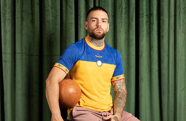 Modelo Reebok Jerseys Retro con jersey amarillo y azul, escudo retro, bal&oacute;n vintage, fondo cortina verde.
