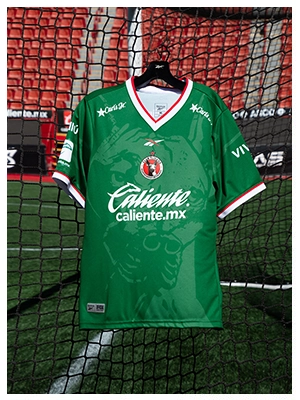 Reebok x Xolos en jersey verde frente a la porter&iacute;a rojo del club.