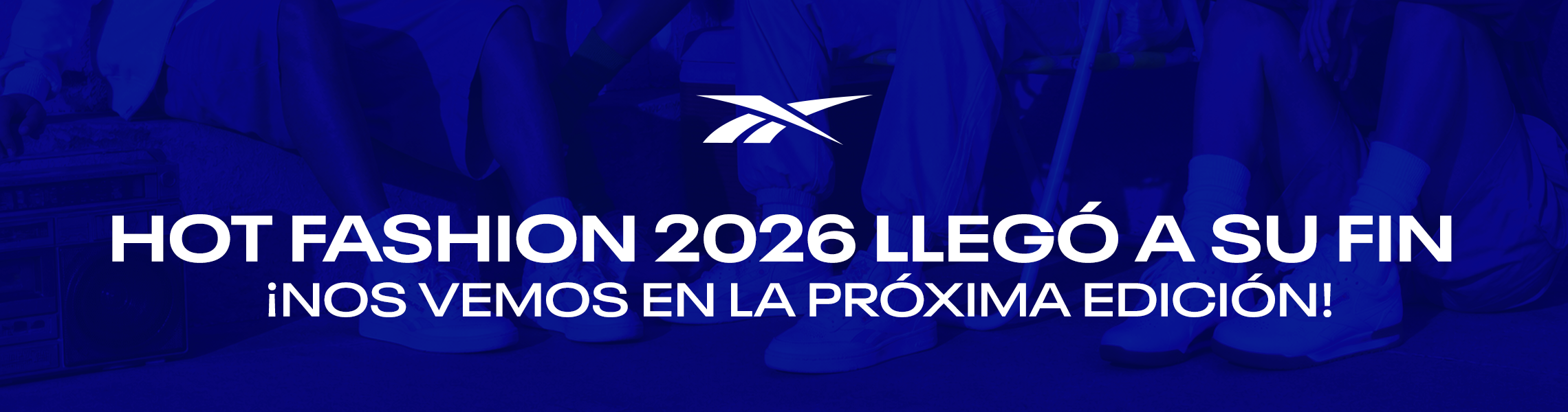 Banner desktop home Reebok Hot Fashion 2026 lleg&oacute; a su fin, fondo azul intenso con grupo de personas sentadas mostrando pants y tenis Reebok, logo Reebok Vector blanco centrado, texto Hot Fashion 2026 Lleg&oacute; a su Fin, Nos Vemos en la Pr&oacute;xima Edici&oacute;n. Hot Fashion Reebok, cierre Hot Fashion, ofertas Reebok y descuentos Reebok en ropa y tenis