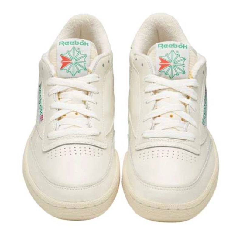 Recuadro de producto Reebok Club C 85 en color crema vistos de frente sobre fondo blanco, con logo Reebok Starcrest verde y rojo en la leng&uuml;eta y piel perforada, campa&ntilde;a Reebok x Karol G Born Classic. Reebok, Karol G, Club C 85, tenis blancos Reebok, Reebok Classics y Born Classic Worn For Life.